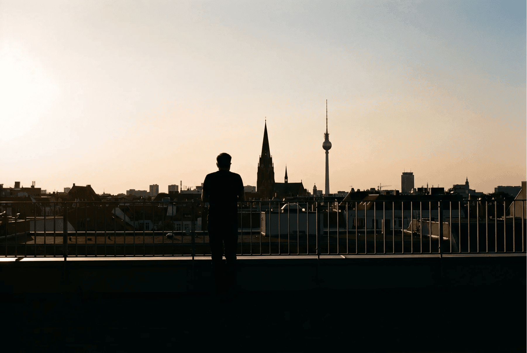 Friedrich Berlin – Person silhouettiert auf einer Dachterrasse mit Blick auf die Berliner Skyline mit Fernsehturm im Sonnenuntergang