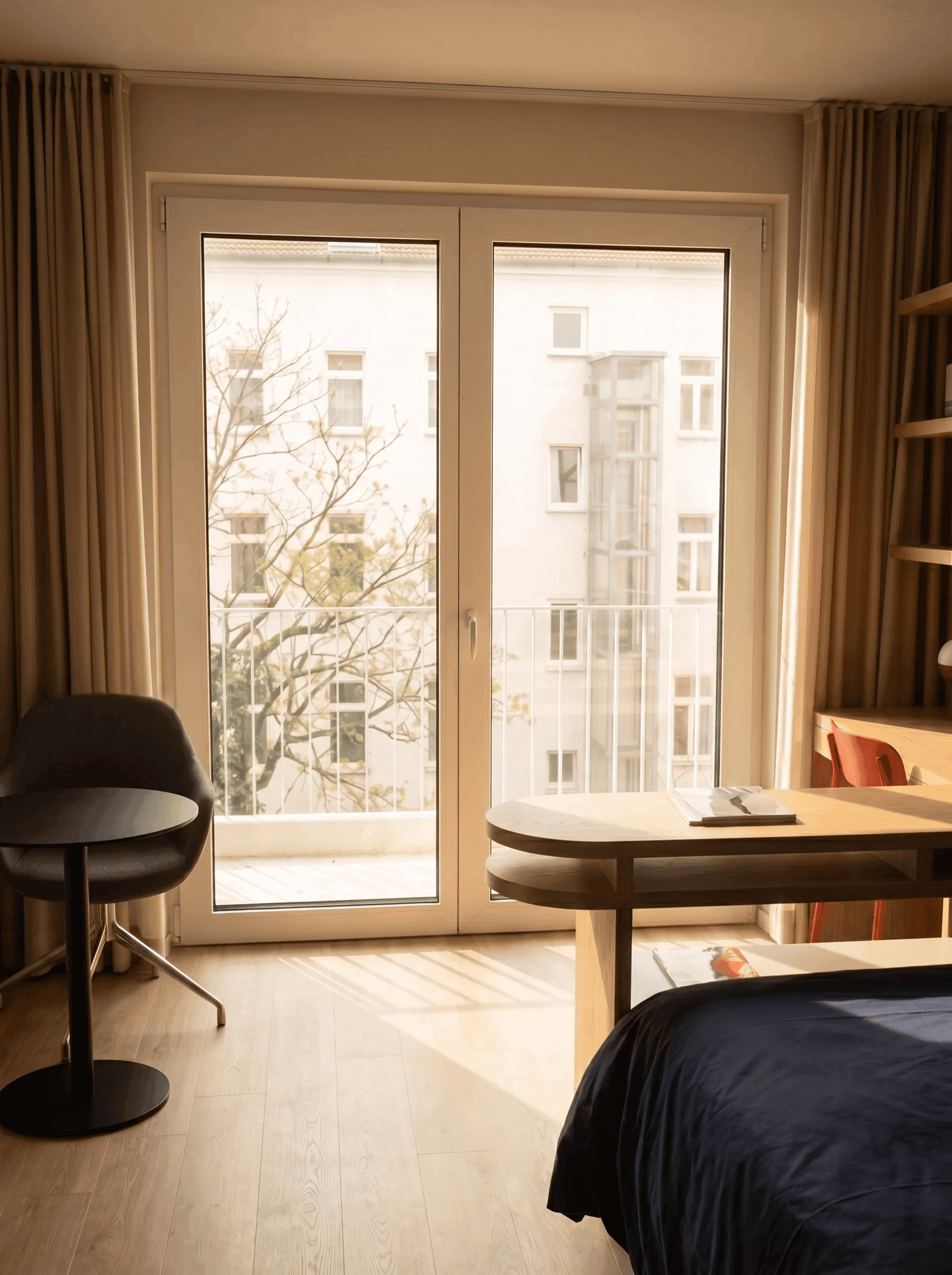 Friedrich-Apartment Blick zur Balkontür: sonnendurchflutetes Zimmer mit offener Balkontür, Ausblick auf Berliner Altbauten und Baumkronen, Schreibtisch und Bett im Vordergrund