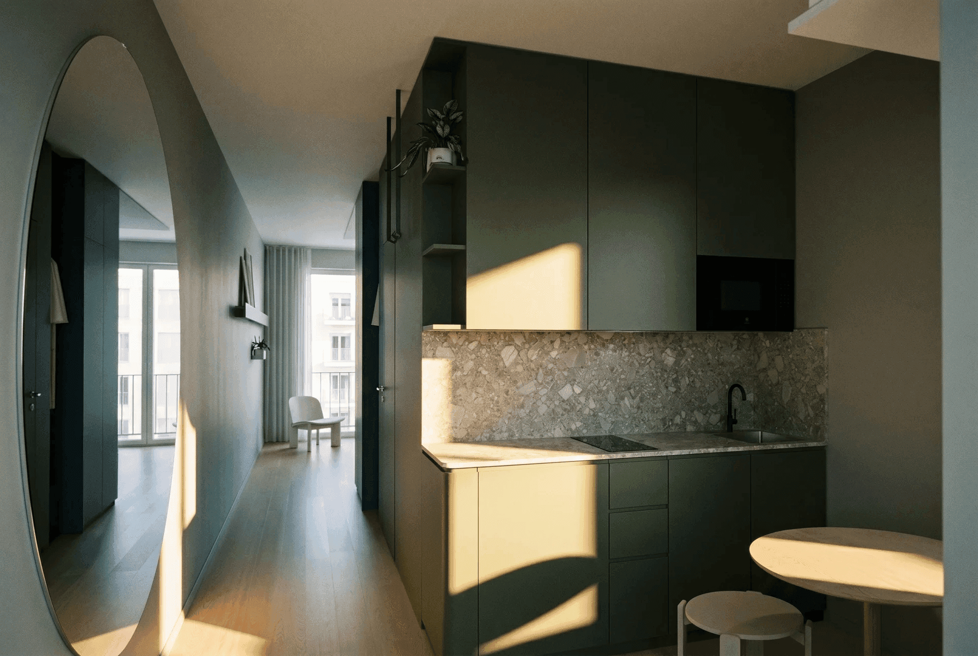 Friedrich Studio Compact Küche: dunkelgrüne Fronten mit Terrazzospritzschutz, runder Wandspiegel im Flur, Blick in den hellen Wohnraum mit Balkon