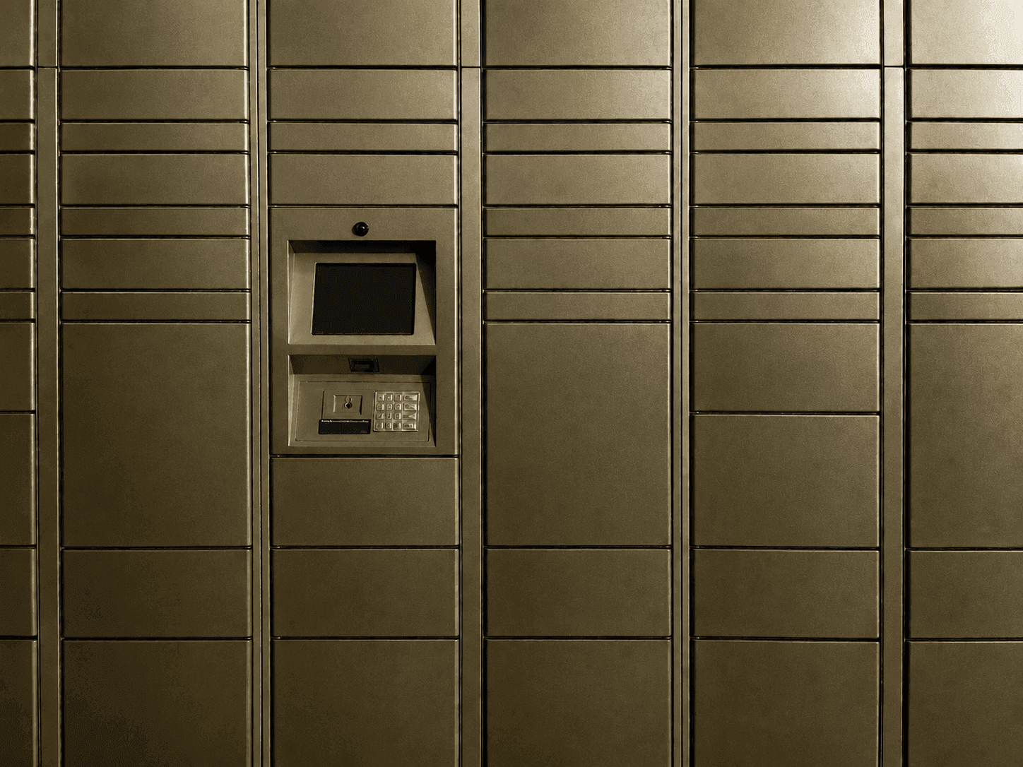 Reihen bronzefarbener Paketschließfächer mit zentralem Touchscreen-Bedienterminal und Zahlentastatur